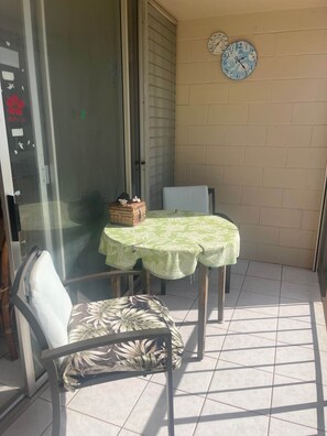 Een klein balkon met een tafel en stoelen, een klok aan de muur en een schuifdeur.