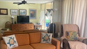 A living room with a sofa, armchair, TV, ceiling fan, and artwork on the wall. - Kihei Beach Stay at Hale Kai O' Kihei - Oceanfront in Maui (Kihei)