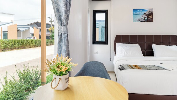A hotel room with a bed, a window, a view of the ocean, a potted plant, and a table. - Deluxe Hotel Chaiyaphum (Chatturat)