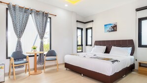 A bedroom with a bed, two chairs, a small table, and a window with curtains. - Deluxe Hotel Chaiyaphum (Chatturat)