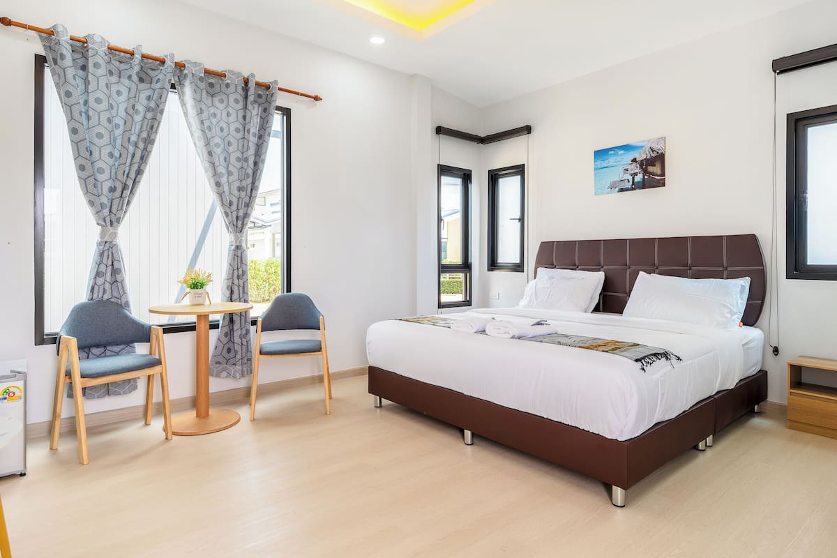 A bedroom with a bed, two chairs, a small table, and a window with curtains.