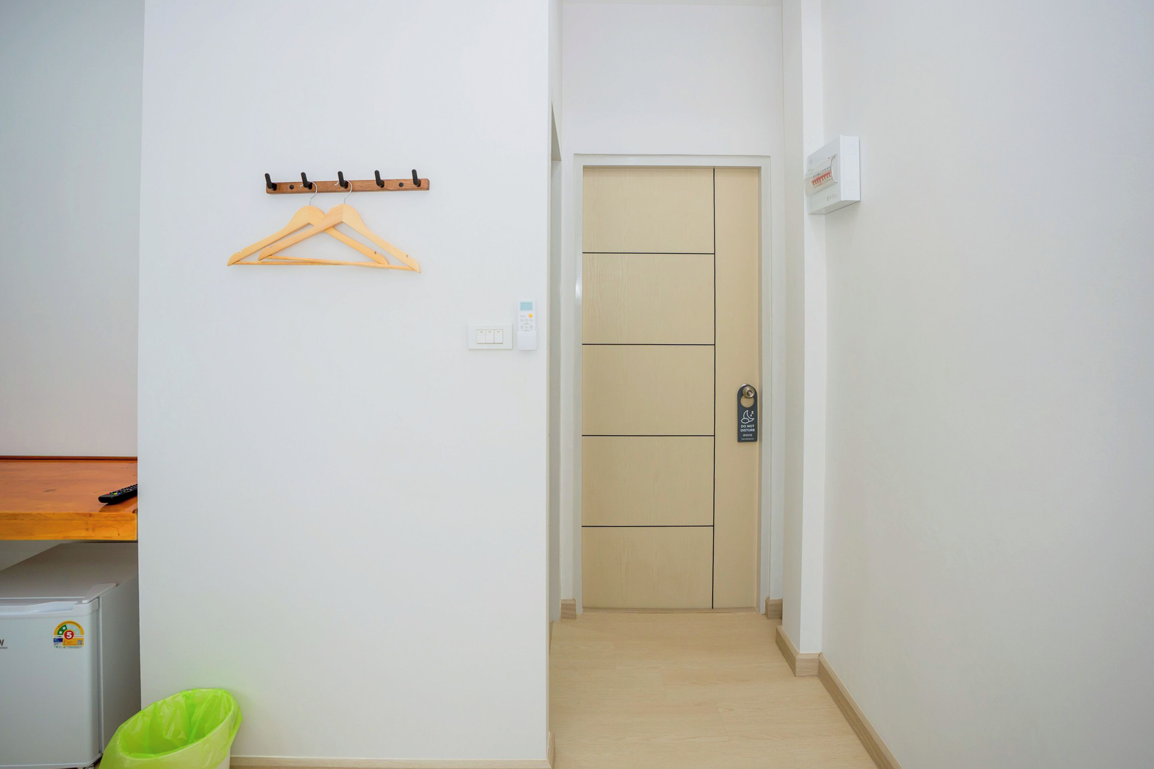 A hallway with a wooden door, a coat rack, a small trash bin, and a light switch.