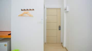 A hallway with a wooden door, a coat rack, a small trash bin, and a light switch.
