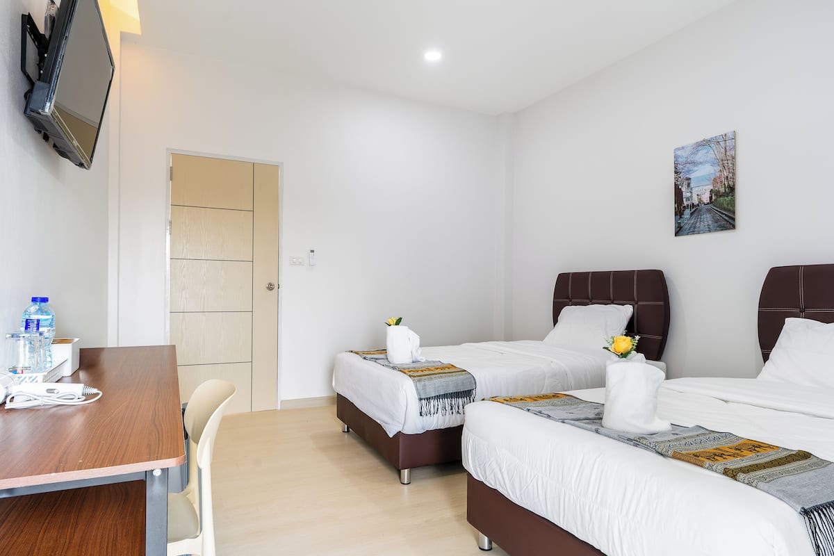 A hotel room with two beds, a desk, a chair, and a TV mounted on the wall.