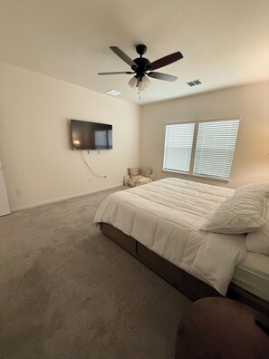 Quarto com uma cama, um ventilador de teto, uma televisão e duas janelas com persianas.