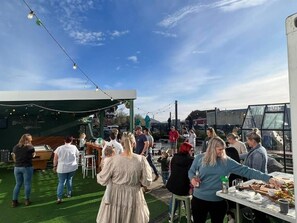 Un événement en plein air où les participants sont rassemblés autour de tables, sur une pelouse artificielle verte, sous un ciel dégagé.