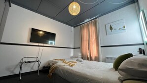 A hotel room with a bed, a television mounted on the wall, a standing lamp, and a window with curtains. - Railway Hotel Winton (Winton)