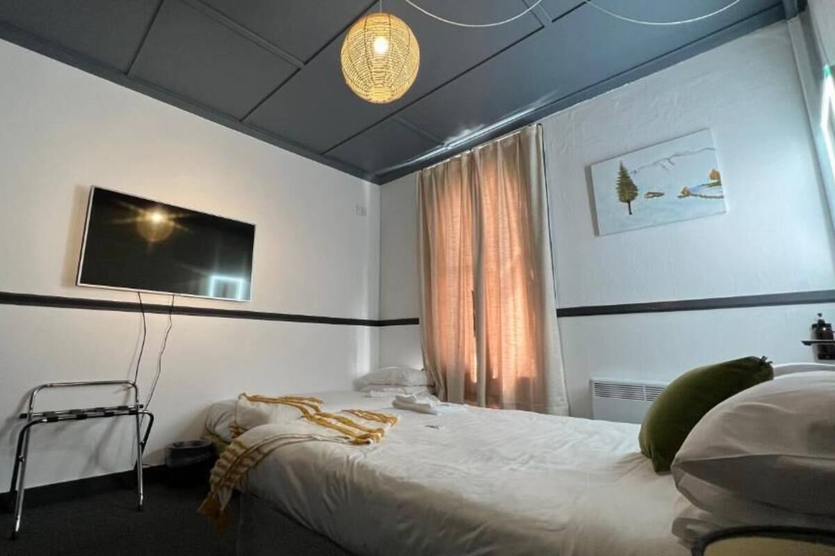 A hotel room with a bed, a television mounted on the wall, a standing lamp, and a window with curtains.