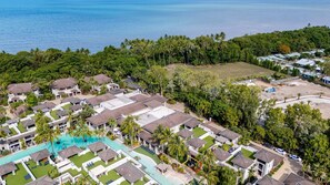 An aerial view of a resort with multiple bungalow-style buildings, a central swimming pool, and a backdrop of dense tropical vegetation and the ocean. - 103 Temple By The Sea (Craiglie)