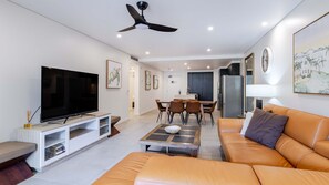 Un salon moderne doté d’un téléviseur à écran plat, d’un ventilateur de plafond, d’un coin repas et d’une cuisine en arrière-plan.