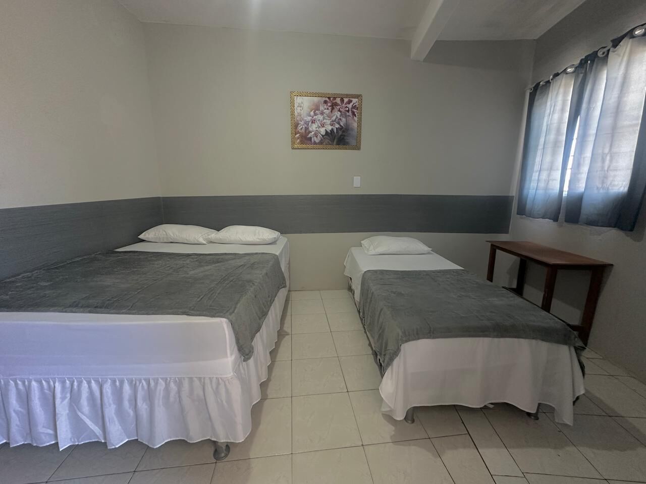 A room with two beds, a small table, and a painting on the wall.