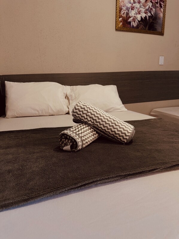 A bed with white pillows, a dark brown headboard, and a patterned throw blanket.