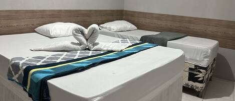 A hotel room with a bed, a small bedside table, and a wall-mounted light switch.
