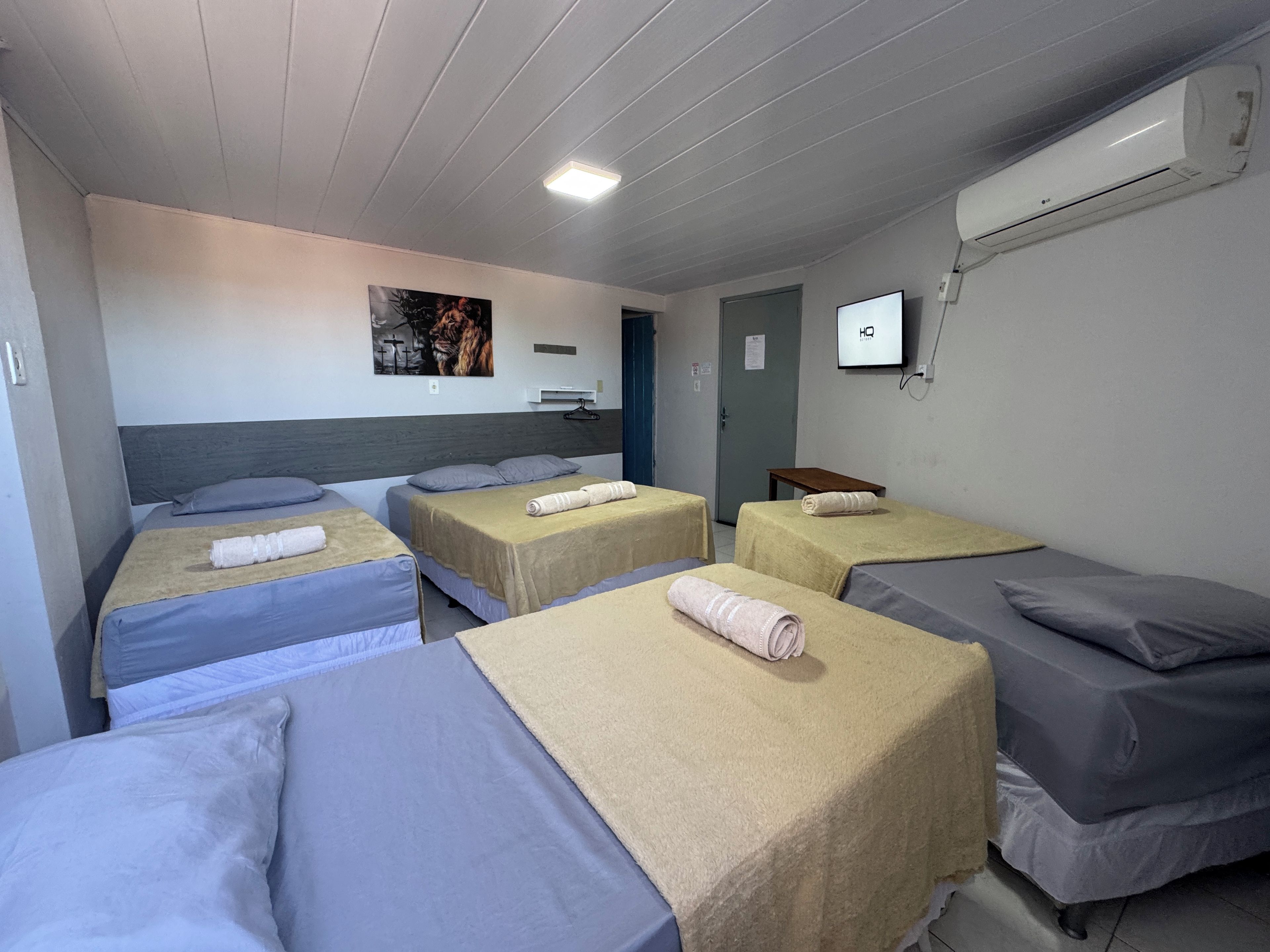 Quarto de hotel com quatro camas, uma TV na parede e um aparelho de ar condicionado.