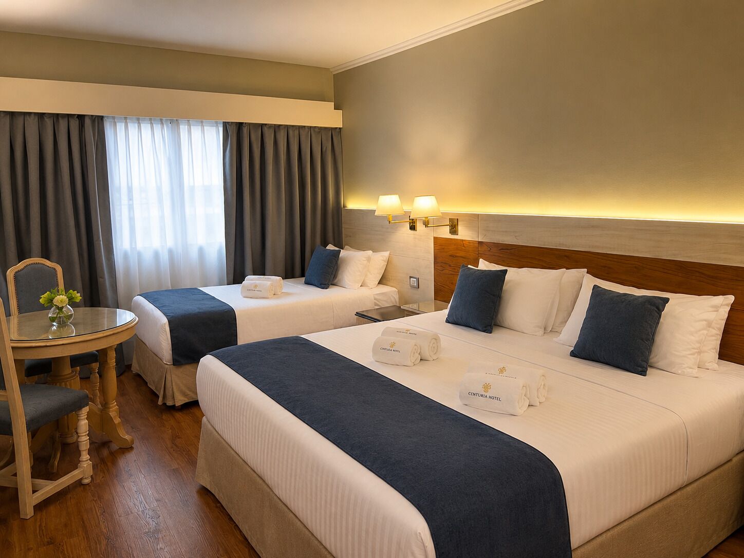 A hotel room with two beds, a small table, and a chair.