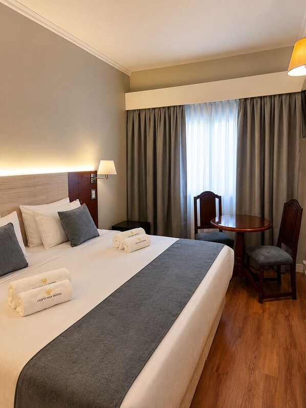 A hotel room with a large bed, a bedside table, a chair, a small table, and a lamp. - Centuria Obelisco Hotel (Buenos Aires)