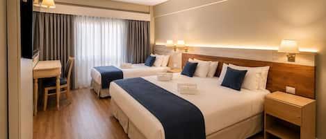 A hotel room with two beds, a desk, and a TV.