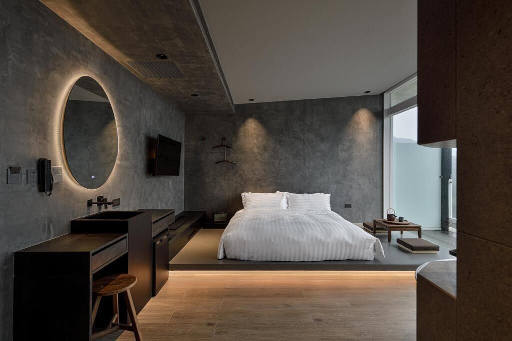 A modern bedroom with a large bed, a built-in desk, a round mirror, and a large window.