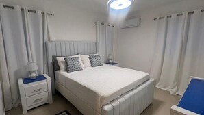 A bedroom with a bed, nightstands, a lamp, curtains, and a ceiling light fixture.