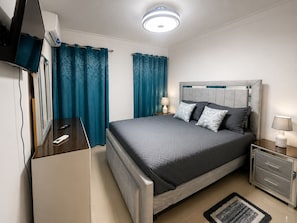 A modern bedroom with a bed, bedside tables, a TV, and curtains.