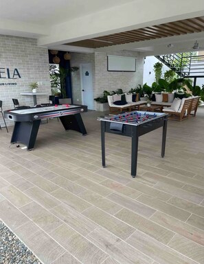 Ein Billardtisch, ein Kicker und eine Sitzecke mit Sofa, einer Ziegelwand und Pflanzen.