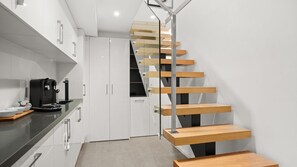 A modern kitchen with a built-in coffee maker, white cabinets, and a wooden staircase. - Albertine House - beautiful single-fronted weatherboard Victorian home i (Albert Park)
