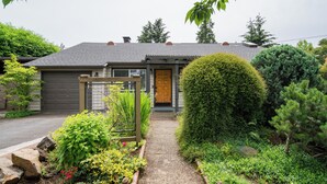 A residential house with a front door, a garage, and a well-maintained garden with various plants and a pathway.