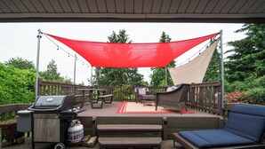 An outdoor deck with a grill, seating, and a shaded area.