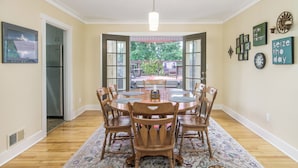 A dining room with a round table, wooden chairs, a chandelier, and a view through open doors to an outdoor patio.