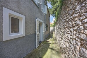 Een smalle steeg met een stenen muur aan de ene kant en een gebouw met een raam en een deur aan de andere kant.
