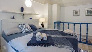 Una cama bien hecha con toallas enrolladas, una lámpara de noche y un estante en la pared con adornos.