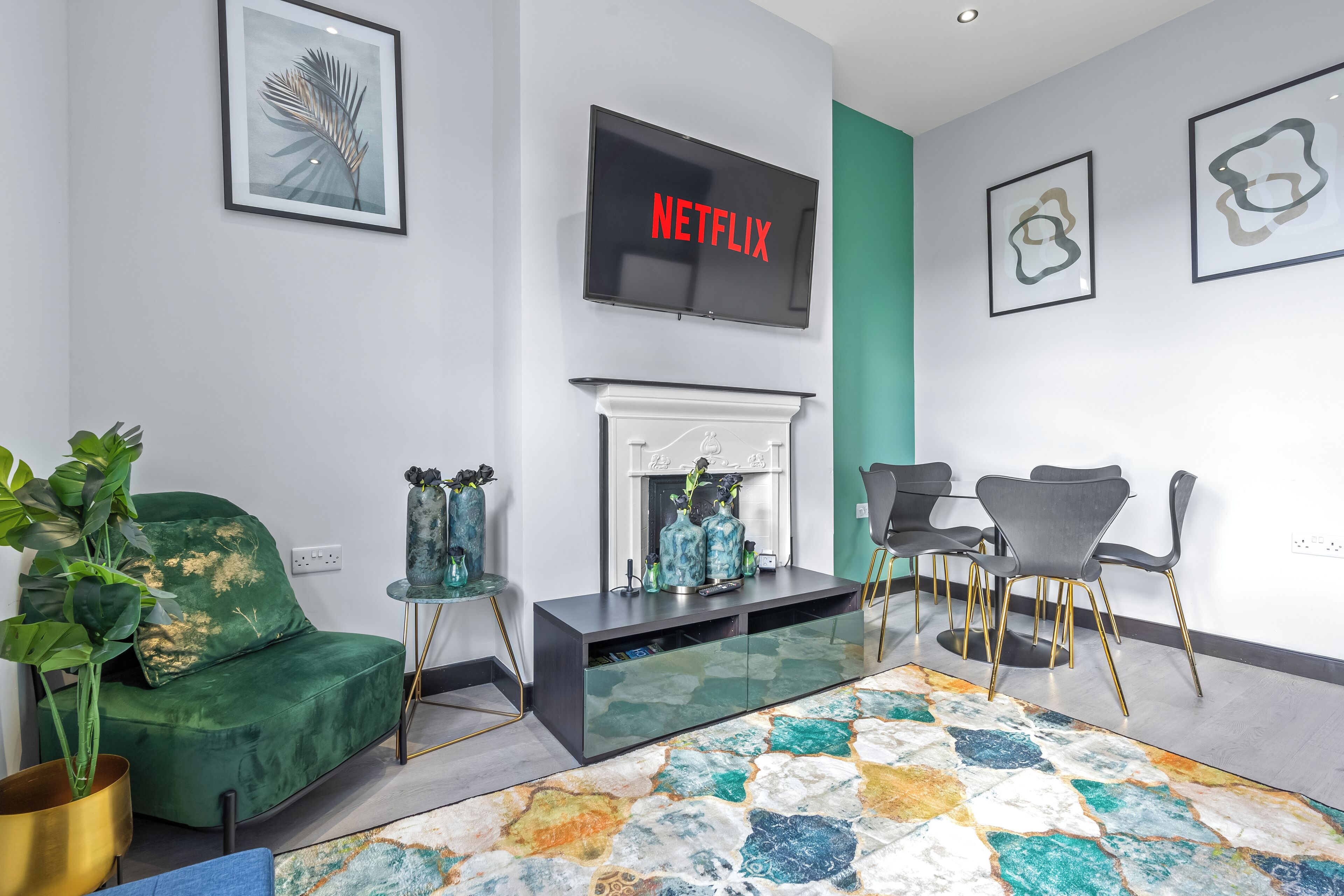 A modern living room with a green sofa, a fireplace, a flat-screen TV, and a colorful rug.