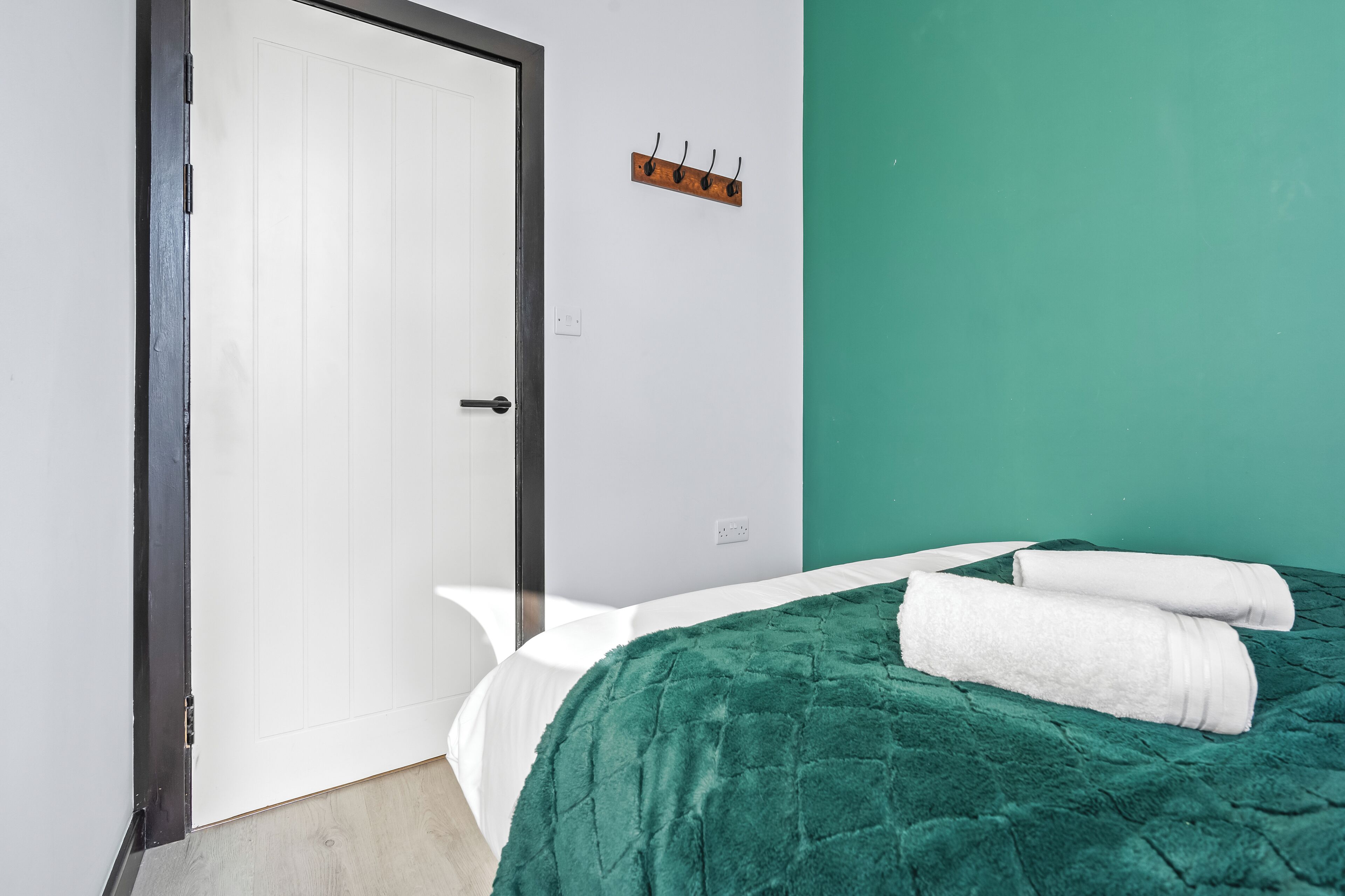 A room with a bed, a white door, a green wall, and a coat rack.