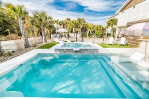 Una piscina con un jacuzzi, rodeada de palmeras y una cerca blanca.