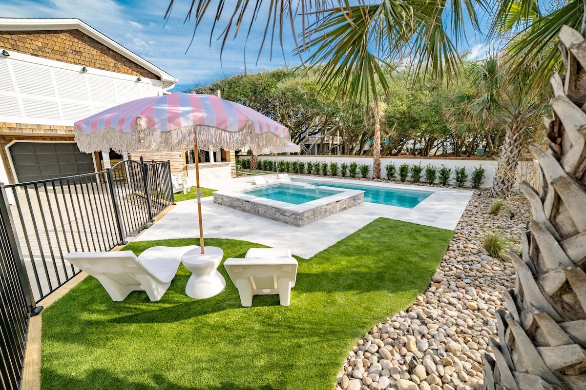 A backyard with a swimming pool, two lounge chairs, and a tiki-style umbrella.