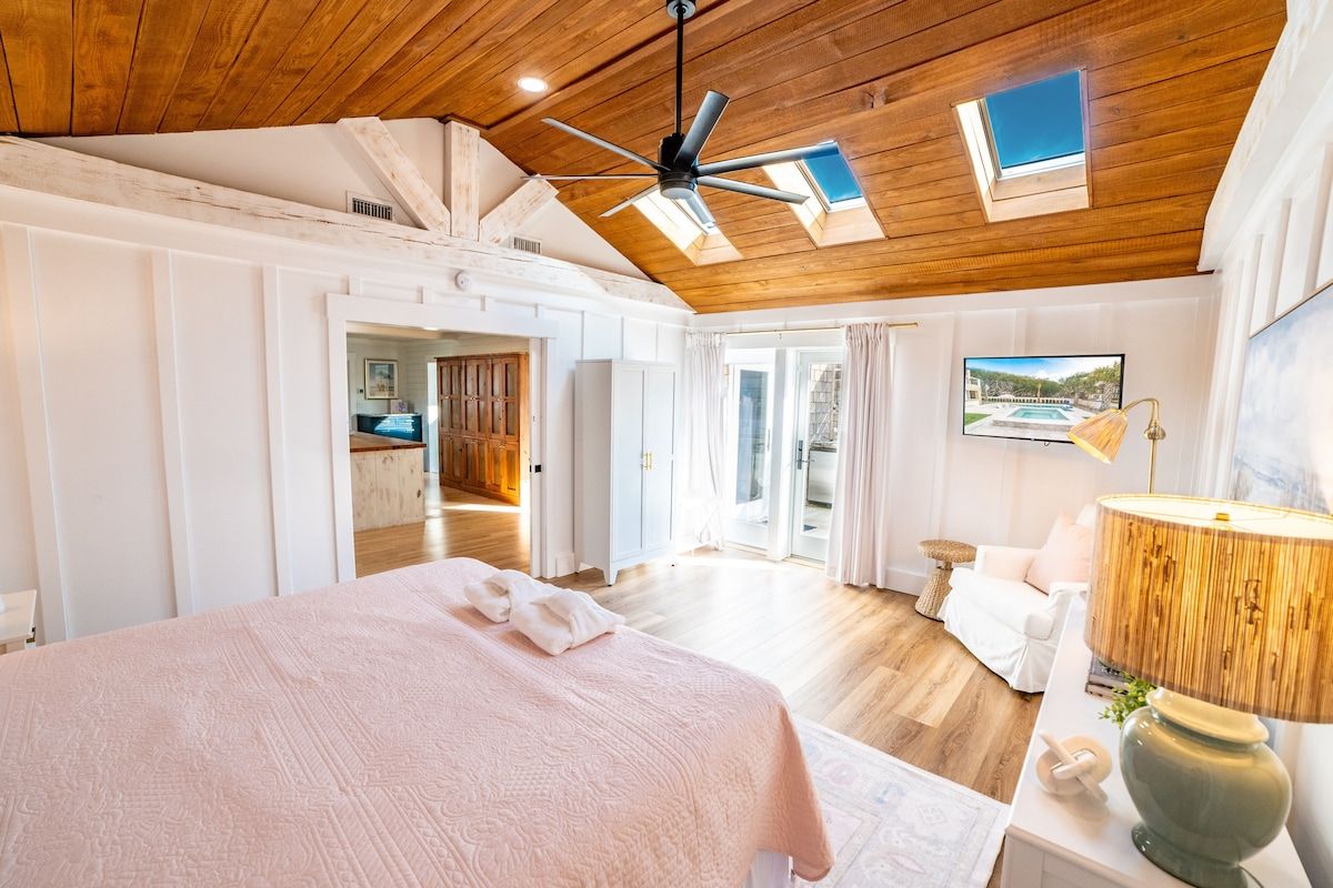 Un dormitorio con una cama grande, ventilador de techo, tragaluces, televisor y una lámpara.