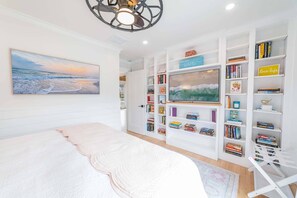 Une chambre à coucher avec un grand lit, une bibliothèque, un téléviseur et un tableau représentant une scène de plage.