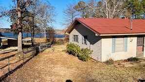 Une maison de plain-pied avec un toit rouge, une cour clôturée et une vue sur un lac.