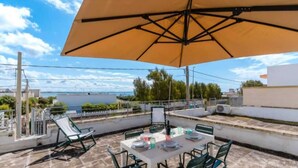 Eine Terrasse mit Esstisch, Gartenmöbeln und einem großen Sonnenschirm.