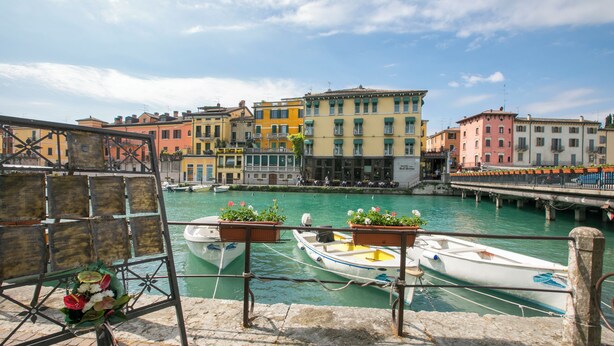 Un canale con barche ormeggiate, edifici lungo l'acqua e un ponte sullo sfondo.