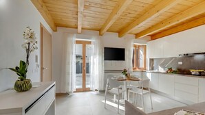 Una cucina moderna con mobili bianchi, un frigorifero in acciaio inossidabile e un televisore a schermo piatto montato sopra il bancone.