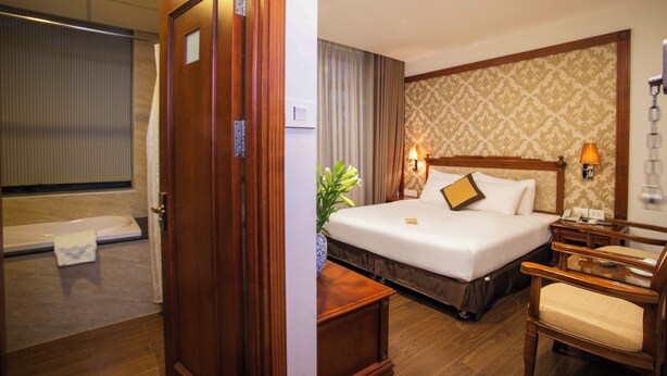 Una habitación de hotel con cama, mesita de noche, silla y un baño con bañera.
