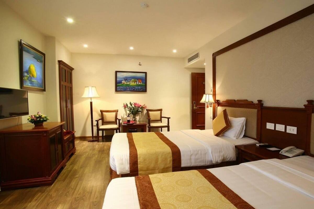 A hotel room with two beds, a desk with a lamp, a TV, and a painting on the wall.