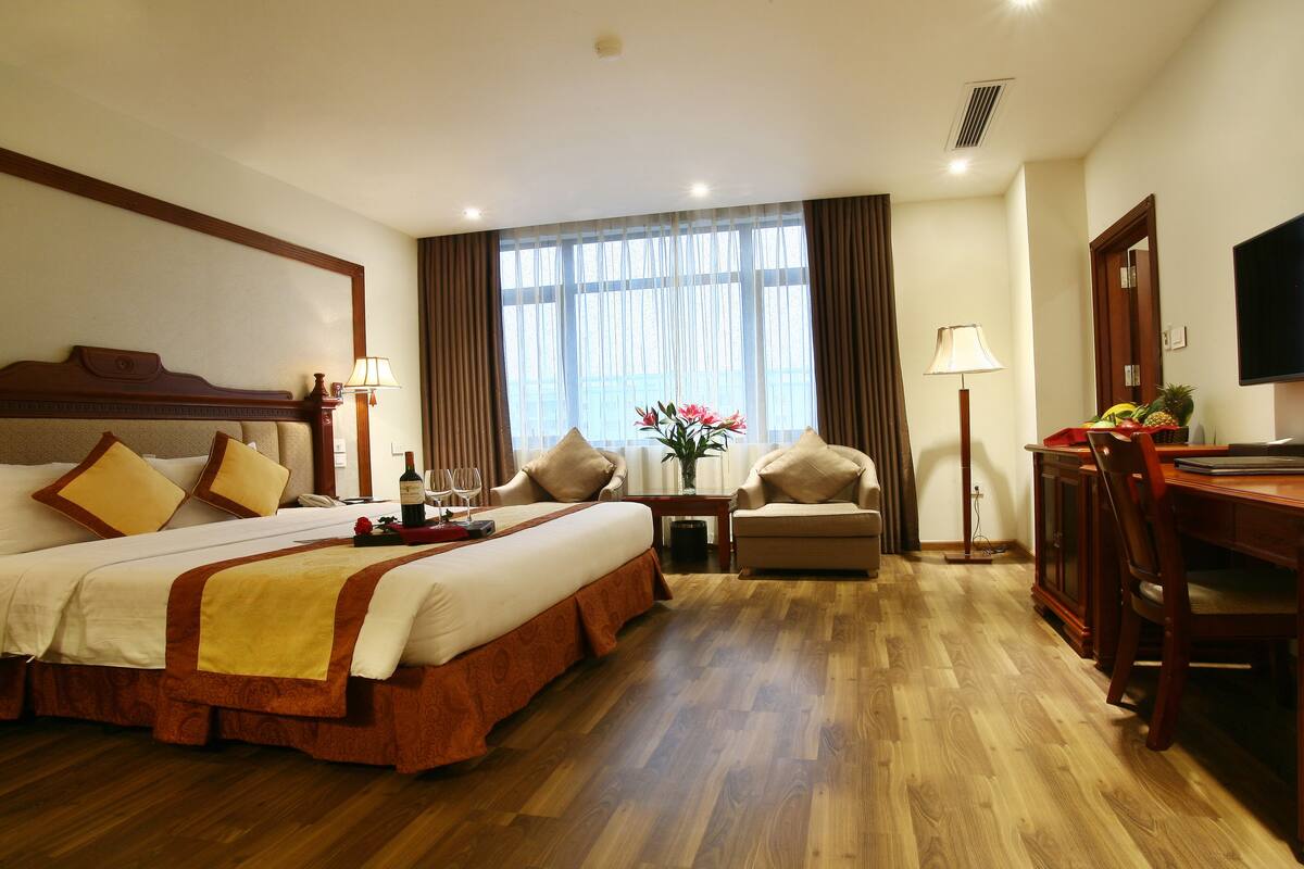 A hotel room with a large bed, a desk, a chair, a TV, and a window with curtains.