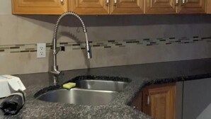Cucina con mobili in legno, piano di lavoro in granito, lavello in acciaio inox e lampada a sospensione.