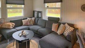 Moderni olohuone, jossa on harmaa kulmasohva, pieni sohvapöytä ja suuri ikkuna, jossa on sälekaihtimet.