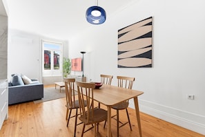 A modern dining area with a wooden table and chairs, a blue pendant light, and a 'GUEST READY' sign. - GuestReady - Beautiful studio in Porto's heart (Porto)