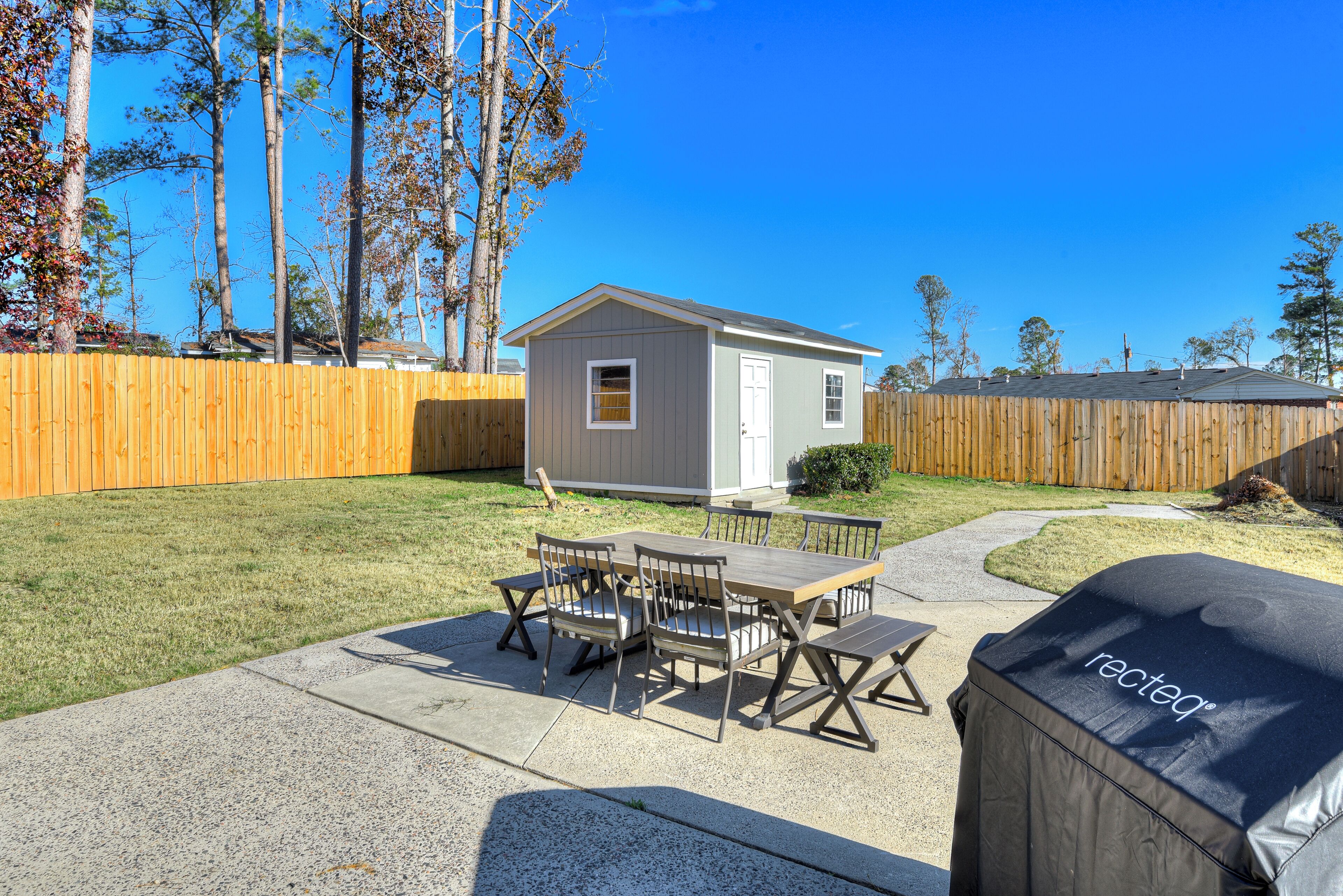 A backyard with a wooden table and chairs, a barbecue grill, and a small shed.