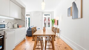 Una cocina moderna con armarios blancos, una mesa de comedor de madera y vistas al exterior a través de una puerta de cristal.