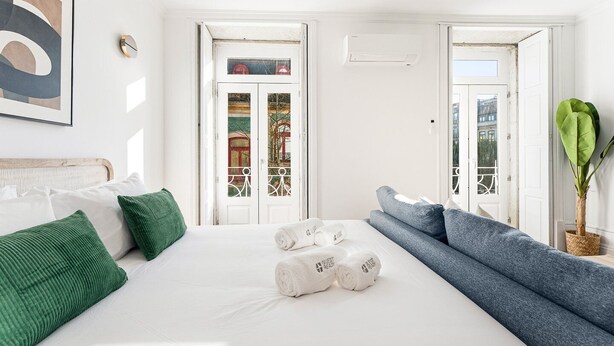 Habitación de hotel con cama, sofá, planta en maceta y vistas por la puerta.